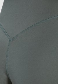 Primer plano de leggings deportivos de color verde oscuro que muestran una tela suave y elástica con un patrón acanalado texturizado y detalles de costura en contraste.