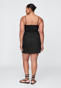 Čierne šaty s nariaseným živôtikom, tenkými ramienkami a voľným strihom. Kombinované s čiernymi sandálmi na remienky. Hladká textúra látky.