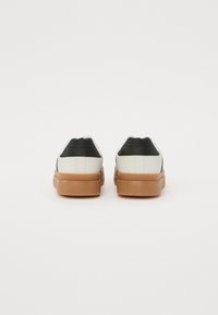 Adidași albi și negri cu talpă din cauciuc, având un superior din material sintetic neted, un panou la călcâi în contrast și detalii discrete de cusătură.
