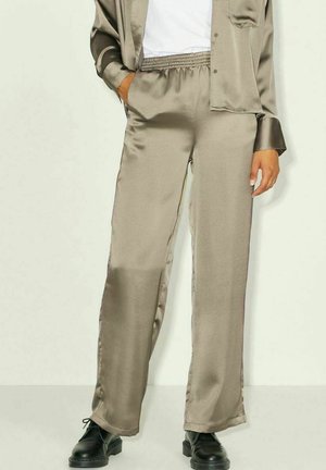 Pantalon beige en satin avec une ceinture élastique, des poches latérales et une coupe décontractée, associé à une chemise assortie et des chaussures noires.