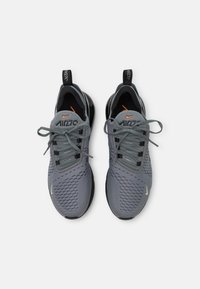 Ett par grå Nike Air Max 270 sneakers med svarta och orange detaljer, snörda, sedda ovanifrån mot en vit bakgrund.