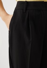 Zwarte broeken met een gladde textuur, voorzien van zijzakken, een platte voorkant en een aansluitende tailleband. Tailored ontwerp dat comfort benadrukt.