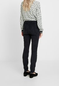 Czarne slim-fit spodnie o gładkiej fakturze. W zestawieniu z bluzką w wzory z wirującymi wzorami. Akcesoria to czarne buty.