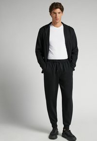 Czarna bluza z kapturem na zamek, pod którą znajduje się biała koszulka, oraz czarne dresy. Strój jest swobodny, z elastycznym pasem i kieszeniami.