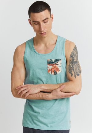Light blue tank top in soft fabric with a chest pocket featuring a tropical leaf print. Simple, relaxed design with a crew neckline.