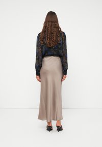 Maxi gonna beige setosa abbinata a un blouse nero trasparente con motivi floreali blu, vista da dietro.