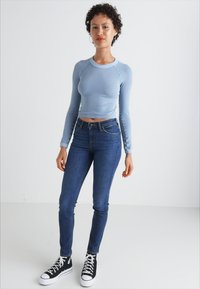 Haut bleu clair à manches longues, court, associé à un jean skinny bleu foncé et des baskets montantes noires. Matière lisse, design ajusté, détails minimalistes.