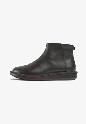 Stivale alla caviglia in pelle nera con punta arrotondata, suola piatta con una sottile striscia rossa e linguetta sul retro, mostrato in profilo laterale su sfondo bianco.