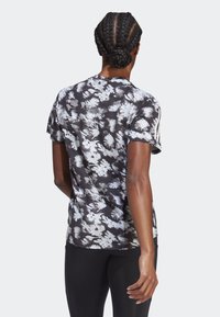 Camiseta deportiva de manga corta y cuello redondo en negro con patrones florales blancos y tejido texturizado; presenta franjas laterales de contraste.