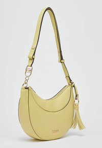 Sac à bandoulière en similicuir jaune avec une forme arrondie, des finitions noires, des détails en métal doré et un pompon. Il est doté d'une fermeture éclair et d'une sangle réglable.