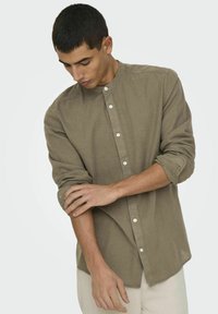Camicia in lino khaki con colletto alla coreana e chiusura a bottoni, con maniche arrotolate e un taglio rilassato. Tessuto liscio con una leggera lucentezza.