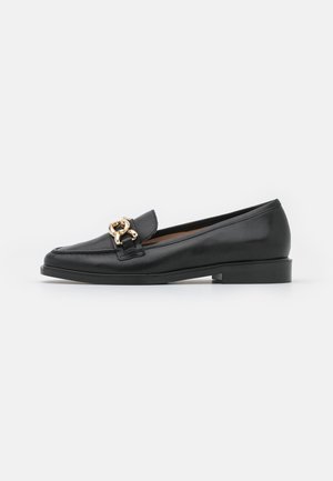 Zwarte leren loafers met een ronde neus en een lage hak, voorzien van een gouden metalen accent aan de voorkant. Gladde textuur en klassiek ontwerp.