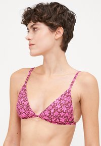 Top de bikini triangulo rosa com flores, com tiras finas e um padrão sobre um fundo castanho. Textura suave com hardware mínimo.