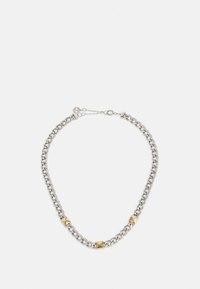 Hopeaketju, jossa on pyramidimuotoiset korostukset ja vuorotellen kultasävytettyjä metallinappeja. Säädettävä lukko pienen jatkoketjun kanssa.