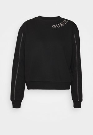 Sweat-shirt noir à manches longues avec le texte "GUESS" en strass sur la partie supérieure de la poitrine et des détails de fermeture éclair argentés courant le long des deux manches.