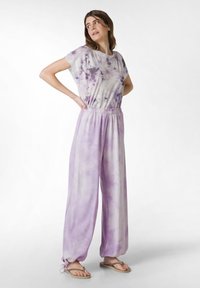 Lila tie-dye jumpsuit med korta ärmar, elastisk midja, vida ben och manschetter. Mjuk tyg med en lätt textur.