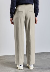 Pantalones beige de pierna ancha hechos de una tela suave, con dos bolsillos traseros, una cintura lisa y un dobladillo recto, combinados con zapatillas blancas.