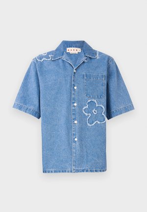 Chemise en denim à manches courtes de couleur bleu clair, ornée de deux motifs floraux effilochés, d'une poche poitrine et de boutons blancs le long de l'avant.