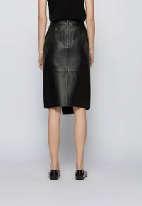 Musta nahkahame, jossa on polven pituinen muotoilu, näkyvät sauma-viivat ja keskiselkäinen vetoketjukiinnitys. Suuri tekstuuri, hienovarainen kiilto.