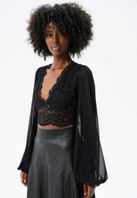 Czarna koronkowa bluzka z dekoltem w serek, długimi przezroczystymi rękawami i falbaniastym wykończeniem; zestawiona z dopasowaną czarną skórzaną spódnicą.