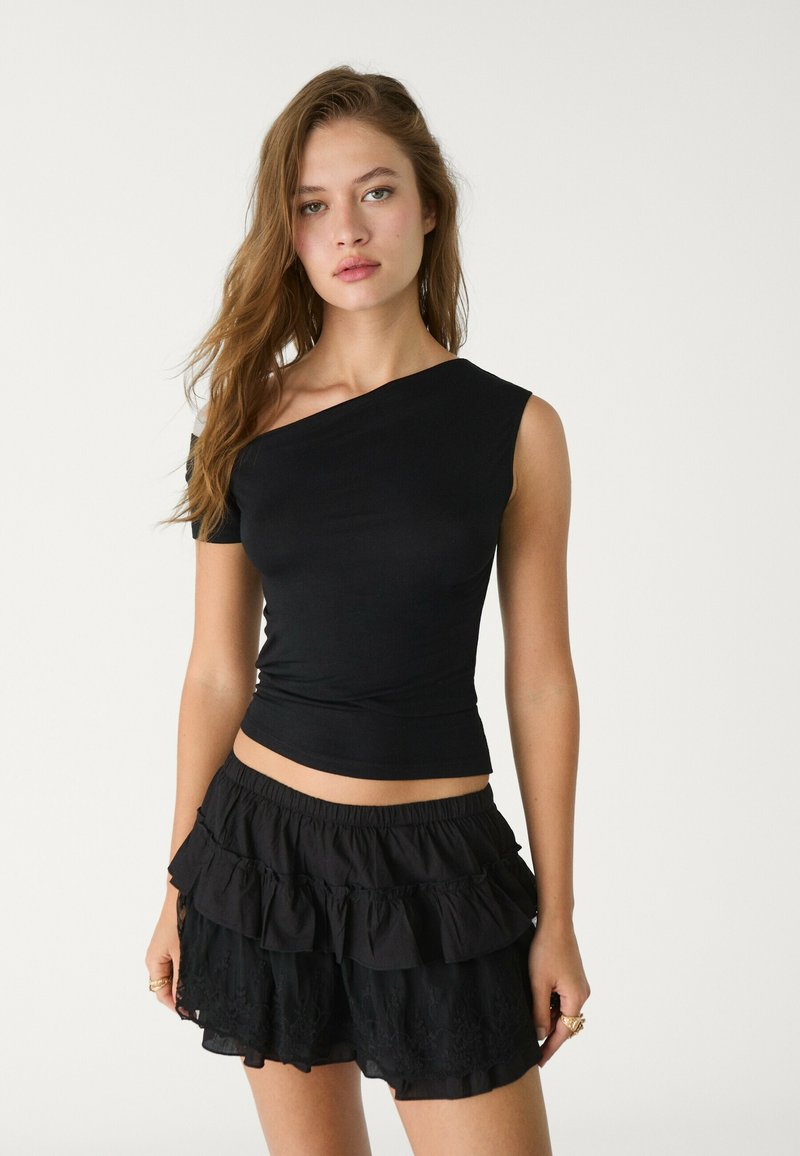 Sort top med én skulder og tætsiddende design, parret med sorte lagdelte shorts med flæser og blondeaccenter. Glat, letvægts stof.