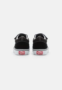Black canvas sneakers with white rubber soles, padded collar, and contrasting white stitching. Features red logo tag on the heel.