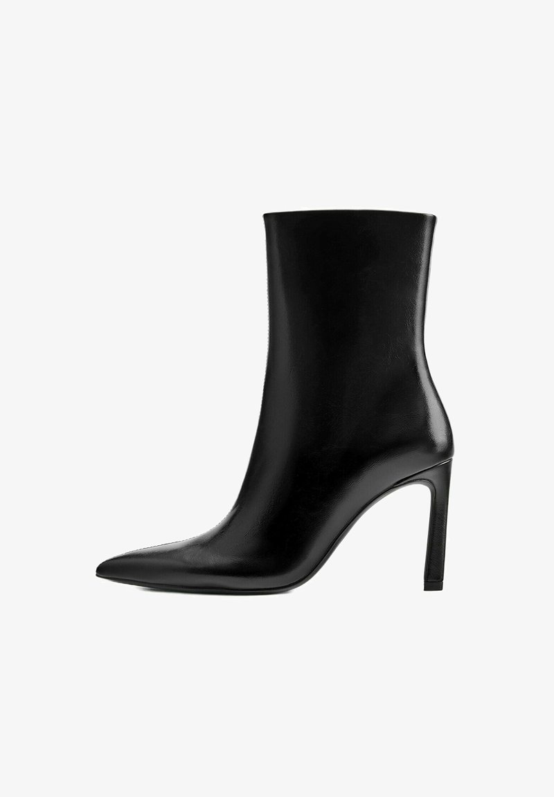 Bottine noire en cuir à talons hauts avec bout pointu et talon aiguille fin sur fond blanc.