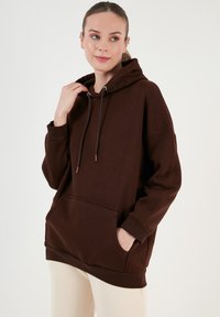 Barna, oversized kapucnis pulóver puha anyagból, elöl zsebbel, állítható húzózsinórral a kapucnin és bordázott mandzsettákkal. Egyszerű, minimalista dizájn.