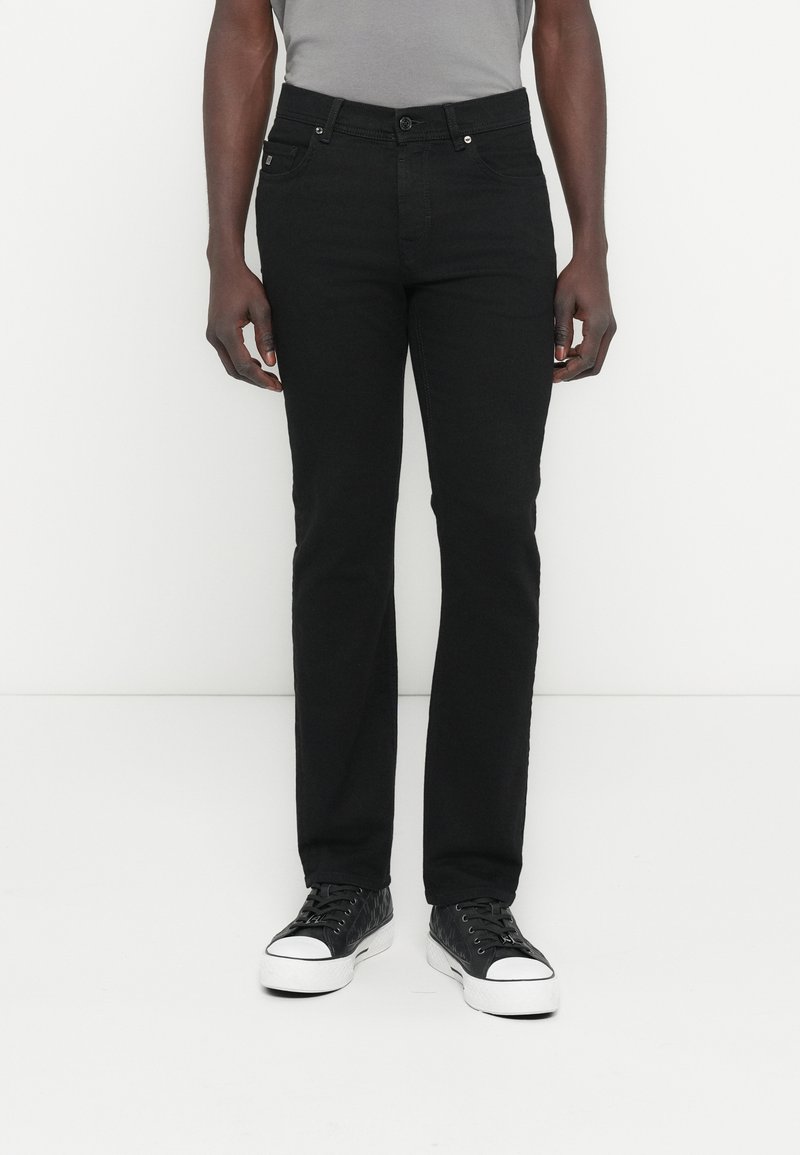 Μαύρο τζιν με στενή γραμμή, σχεδιασμό με πέντε τσέπες, κλείσιμο με κουμπιά και ελάχιστες ασημί λεπτομέρειες. Συνδυάζεται με μαύρα αθλητικά παπούτσια.