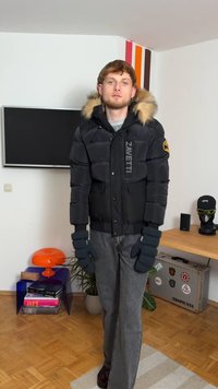 Puffig svart jacka med pälskantad huva och logotyp, kombinerad med mörkgrå byxor och handskar. Varm, isolerad design som passar för kallt väder.