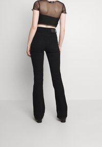 Svarta högmidjade utsvängda jeans med en mjuk textur, två bakfickor och överstygnade sömmar. Kombination med en genomskinlig svart crop top.