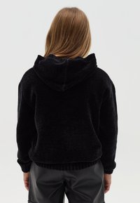 Sudadera negra recortada hecha de tela texturizada, con capucha y dobladillo acanalado. Combinada con pantalones negros de talle alto.