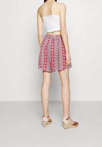 Bílý top bandeau s efektem shlukování a červená sukně s květinovým vzorem. Modelka má na sobě béžové espadrilky na klínku.