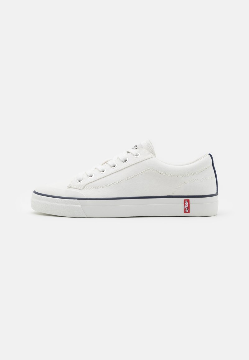 Fehér vászon Sneakers, alacsony profilú dizájnnal, tengerészkék részletekkel a saroknál és a talpnál, valamint hat fűzőlyukkal. Piros logó az oldalon.