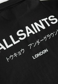 Juodas medvilninis marškinėliai su dideliu baltu tekstu, įskaitant "ALLSAINTS" ir "LONDON", taip pat papildomu tekstu kitomis kalbomis.