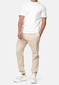 T-shirt bianca a maniche corte abbinata a pantaloni beige a fantasia affusolata, con polsini elasticizzati, e sneakers sportive bianche con dettagli in mesh.