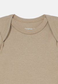 Beige bomullsbody med ribbet halslinning og korte ermer. Stoffet er glatt med en lett tekstur. Merkevarelogo synlig inne i kragen.