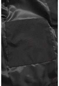 Poche intérieure en tissu noir cousue sur une doublure lisse et brillante, montrant une forme rectangulaire et des détails de couture.