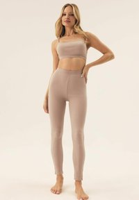 Jasnobrązowy, elastyczny top w stylu crop i dopasowane legginsy o wysokim stanie, bezszwowy design, miękka tekstura, dopasowany krój, długość do kostek.