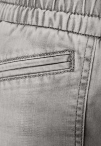 Poche en tissu gris sur un pantalon avec des détails de surpiqûres, une taille élastique et une texture lisse. La poche présente une subtile couture horizontale.