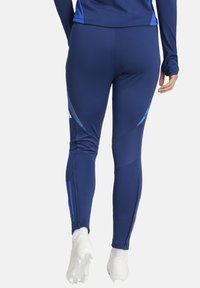 Marinefarbene Sportleggings mit blauen Akzenten, tailliertem Design, strukturierten Einsätzen und Reißverschlüssen an den Knöcheln. Hergestellt aus elastischem, feuchtigkeitsableitendem Material.
