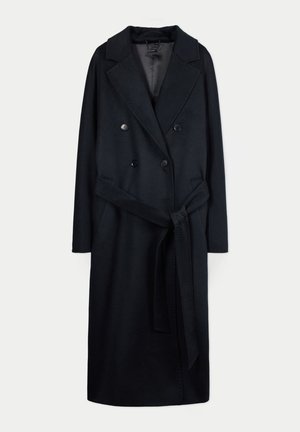 Langer schwarzer doppelseitiger Wollmantel mit breiten Revers und einem Stoffgürtel, der in der Taille auf einem weißen Hintergrund gebunden ist.