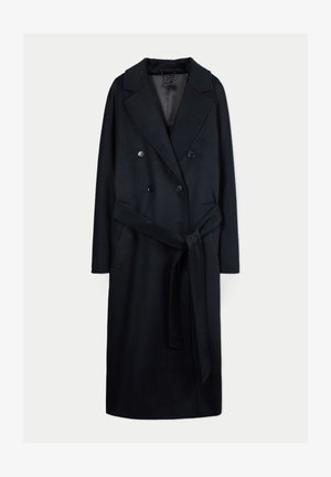 Langer schwarzer doppelseitiger Wollmantel mit breiten Revers und einem Stoffgürtel, der in der Taille auf einem weißen Hintergrund gebunden ist.