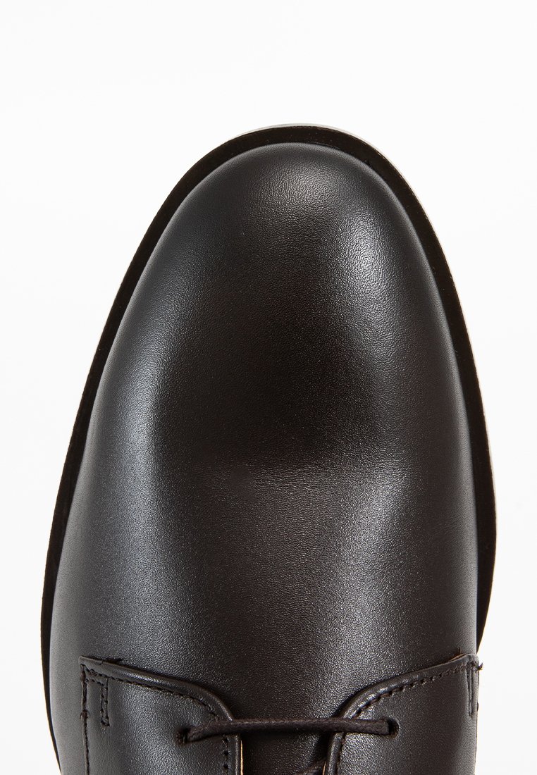 Chaussure habillée en cuir noir avec un bout rond, une texture lisse et des détails de coutures minimaux. Elle dispose d'un système de laçage pour un maintien sécuritaire.