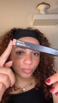 Produkt do konturowania ust w czarnym opakowaniu z różową etykietą, na której widnieje napis "Konturówka do ust" w białym kolorze. Modelka trzyma ołówek blisko twarzy.