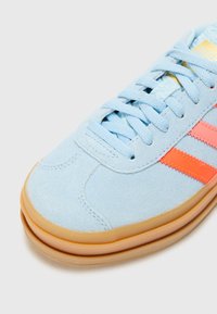 Világoskék velúrbőr sneaker rózsaszín kiegészítőkkel, gumitalppal, kerek orral és lapos fűzővel. Kiemelkedő dizájnja három csíkot tartalmaz.
