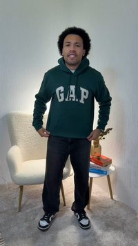 Sweat à capuche vert foncé avec grand lettrage blanc « GAP », poches avant et capuche avec cordon. Porté avec un jean noir et des baskets noires.