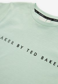 Lys grøn bomulds t-shirt med rund halsudskæring og sort tekst "BAKER BY TED BAKER" trykt hen over fronten i kontrasterende skrifttype.