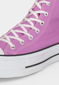 Ροζ πάνινο sneaker ψηλού ποδιού με λευκά κορδόνια, μεταλλικές ραφές, λευκή λαστιχένια σόλα και μαύρη ρίγα.