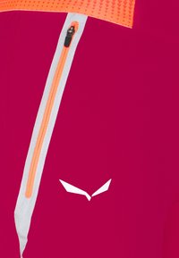 Åtsittande idrottstop i magentafärgad tyg, med en orange dragkedja, grå detaljer och en vit logotyp med en stiliserad design på bröstet.